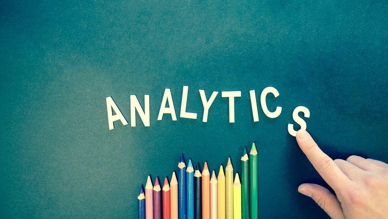 gallery-03 Colored pencils and letters spelling 'ANALYTICS' on a textured background with a hand.
